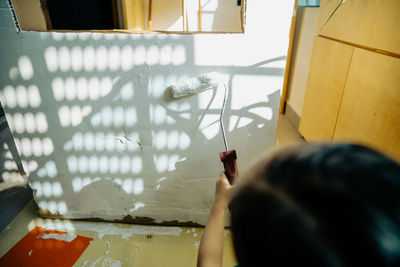 Painting cardboard with white paint and roller by a little girl.