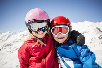 Cheerful siblings in ski-wear standing against snowcapped mountain