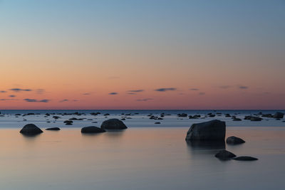 Rocks in sea against sky during sunset