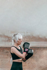 Young woman with arms raised standing against wall