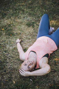 Portrait of smiling woman with head in hand lying down on grass at park