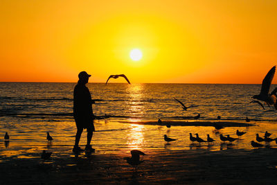 Silhouette people in sea against orange sky