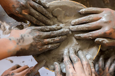 Close-up of people touching mud in container