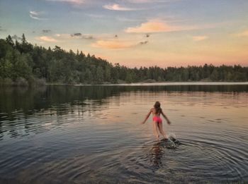 Rear view of girl jumping in lake at sunset