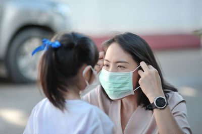 Smiling mother and daughter wearing mask standing outdoors