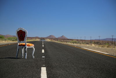 Empty chair on road against clear sky during sunny day