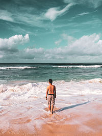 Rear view of shirtless man standing at beach against sky