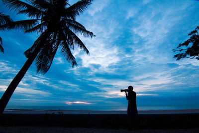 Silhouette man photographing by sea against sky