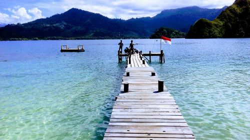 People on pier over lake against sky
