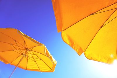 Low angle view of yellow parasols against clear blue sky