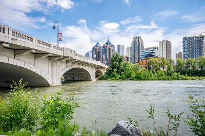 Arch bridge over river by buildings against sky