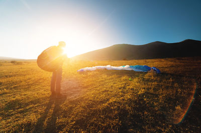 A paraglider takes off from a mountainside with a blue and white canopy and the sun behind. a