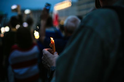 Midsection of protestor holding burning candle during protest at night