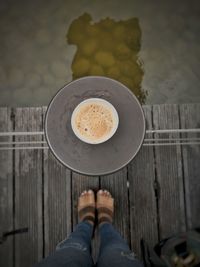 Low section of person standing by coffee cup on pier over lake