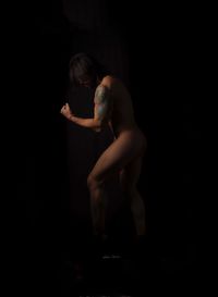 Side view of woman standing against black background