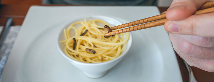 Cropped hand of man having noodles and worms in restaurant