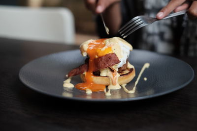 Cropped hand of person having egg's benedict in plate on table