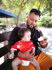 Father holding toy and daughter sitting on bench at beach