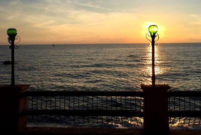 Lamp posts on railing against sea during sunset