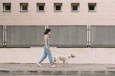 Full length of girl and dog walking on street against building