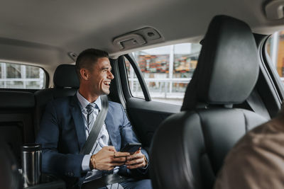 Happy businessman looking through window while sitting in taxi