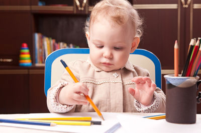 Cute girl holding pencil on table