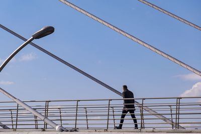 Low angle view of man standing by railing against sky