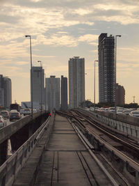 Railroad tracks amidst buildings in city against sky during sunset