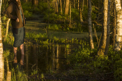 Midsection of woman standing in lake against trees at forest