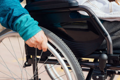 Cropped unrecognizable elderly female in wheelchair riding along embankment near sea and enjoying summer day