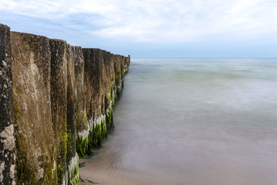 Wooden breakwater covered with moss, arranged in a row at sea, long exposure time, blurred sea waves