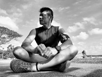 Young man looking away while sitting on land against sky