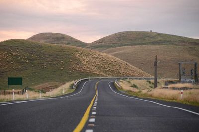 Empty country road leading towards mountains against sky