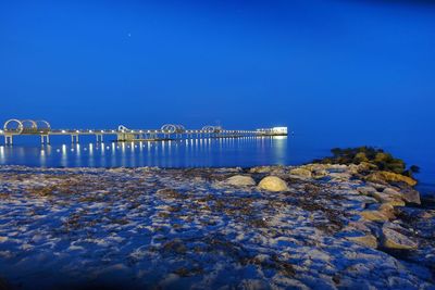 Illuminated bridge over sea against clear blue sky at night