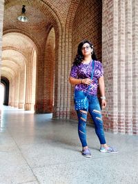 Full length portrait of woman standing at corridor of building