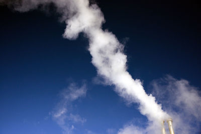 Low angle view of smoke emitting from chimney against blue sky