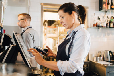 Owner using computer while holding credit card reader in restaurant