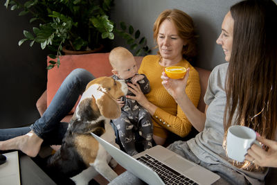 Happy family - grandmother, daughter, newborn baby and dog rest in the living room on the couch