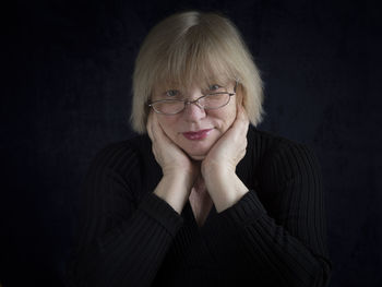 Portrait of mature woman with hands on cheeks against black background