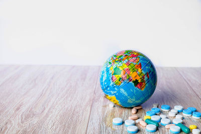 Close-up of globe and medicines on wooden table against white background