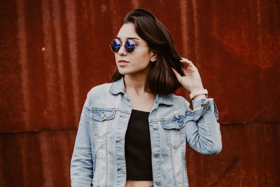 Portrait of young woman wearing sunglasses standing against wall