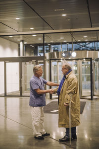 Doctor handshaking with senior patient while standing in lobby of hospital