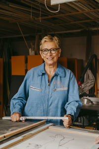 Portrait of smiling senior craftswoman with measuring tape at workshop