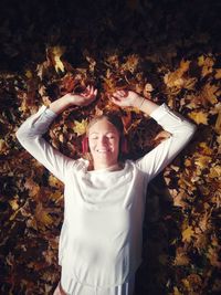 High angle view of woman with eyes closed listening music on autumn leaves