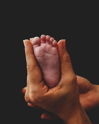 Close-up of human hand anda baby foot against black background 