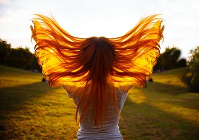 Rear view of woman with tousled hair standing on field