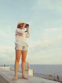 Full length of young woman photographing sea against sky