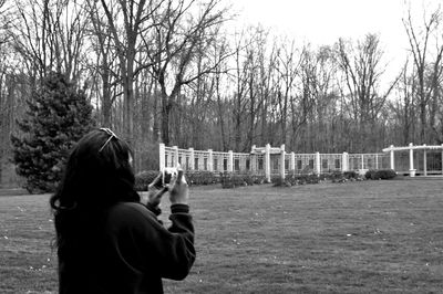Rear view of woman photographing at park against bare trees