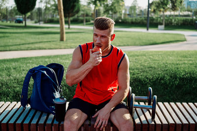 Side view of young man using mobile phone while sitting on bench in park