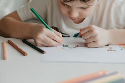 The boy draws with pencils at the kitchen, closeup. high quality photo